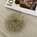 Détail d'un chouchou duveteux en laine vert sauge posé sur un tissu plissé artistique - Chouchou Pelucheux Thé au Lait