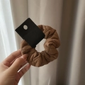 Close-up of brown textured fabric scrunchie with elastic bubble pattern and black card tag - Caramel