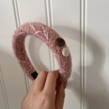 Detailansicht eines rosa Strickstirnbands mit Textur, weißen Nähten und Knöpfen - Rosa