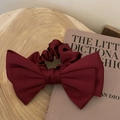 Detail of burgundy oversized satin bow scrunchie on a wood and fashion book background - Red