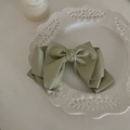 Dettaglio dell'elegante fiocco per capelli in raso verde salvia su piatto di ceramica - Grande Fiocco Irregolare Verde