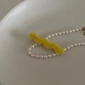 Nahaufnahme einer gelben gewellten Haarklammer und Perlenkette auf einem Keramikteller - Gelb Wellig Mit Buchstaben