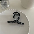 Detail view of marble patterned acetate hair claw clip on a decorative white ceramic plate - Black and White Marble