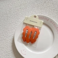 Detail showing set of three orange wavy metal hair clips in retail packaging on a plate - Orange