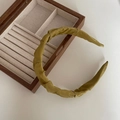 Detail of olive green pleated fabric headband with top knot on a wooden jewelry box - Green