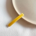 Detail of a minimalist yellow resin hair clip with silver stud on a ceramic plate - Yellow
