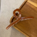 Macro view of amber brown acrylic hair claw clip with cross twisted design and metal spring - Amber Brown