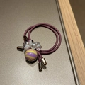Close-up of dual-strand purple hair tie with faceted crystal beads and striped round charm - Purple