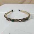 Macro detail of retro golden braided headband with emerald stones and white pearls - Round Emerald Style