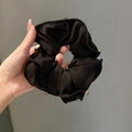Nahaufnahme eines schwarzen Satin-Haargummis mit funkelnden Strasssteinen und Textur - Schwarz