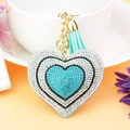 Macro detail of heart-shaped rhinestone keychain with blue tassels and golden bell - Lake Blue