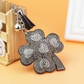 Close-up of sparkling rhinestone clover keychain with silver bell and black tassel detail - Gray