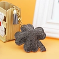 Detailed close-up of dark grey rhinestone clover keychain with golden chain and grey suede tassel - Gray