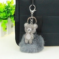 Detail view of a silver rhinestone bear charm with a grey faux fur pompom on a black bag - Gray