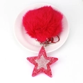 Détail d'un porte-clés à pompon rose avec étoile en strass sur un plateau blanc chic - Rose rouge