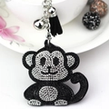 Macro view of rhinestone monkey keychain with black tassel and silver bell detail - Black