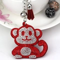 Macro shot of red rhinestone monkey keychain with silver bell and textile tassel charm - Red