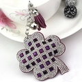 Macro shot of purple four-leaf clover keychain with crystals, leather tassel and silver bell - Purple
