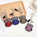 Vue détaillée de quatre porte-clés chouette en cristal avec pompons et clochettes sur bois - Couleur personnalisable