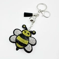 Close-up of cute bee keychain with rhinestones, silver bell and black leather tassel - Yellow