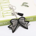 Dettaglio di un portachiavi a fiocco con strass e nappa in pelle nera su un libro - Nero con Bianco