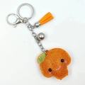 Dettaglio di un portachiavi a forma di frutto con strass e nappa in pelle arancione - Arancia