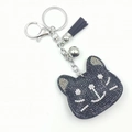 Detail of a sparkling black cat head keychain with silver bells and a black suede tassel - Black