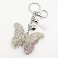 Détail macro du porte-clés papillon avec strass colorés, gland blanc et clochette argentée - Blanc
