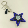 Detail eines sternförmigen Evil Eye Schlüsselanhängers mit blauen Strasssteinen und Quaste - Schwarz