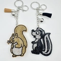 Close-up of squirrel and skunk rhinestone keychains with elegant leather tassels - Custom Color