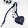 Detail of black leather heart keychain with rhinestone letter L and woven cord - L