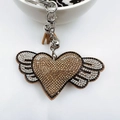Detail eines funkelnden Herz-Flügel-Schlüsselanhängers mit Strass und Lederquaste - Dunkelkhaki
