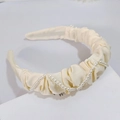 Détail d'un serre-tête en satin plissé crème orné d'élégantes perles blanches sur un socle - Blanc Cassé