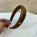 Detalle de la diadema de satén café con una hebilla de metal dorado y grabado - café