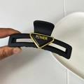 Dettaglio della molletta per capelli nera opaca con decorazione a triangolo e scritta oro - Stile Vuoto