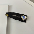 Detalle de la pinza BB de cinta negra con cristal de corazón y logotipo LOVEDAYS oro - Clip BB