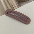 Detail einer matt-violetten hohlen ovalen Haarspange auf einem schlichten weißen Grund - Camel