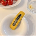 Close-up of yellow faux leather hair clip with fine stitching inside a white ceramic bowl - Yellow