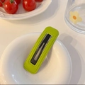 Detail of bright green PU leather hair clip with contrast stitching in a ceramic bowl - Green