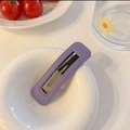 Detailed view of purple leather textured BB hair clip with elegant stitching on white plate - Purple