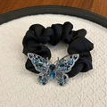 Black velvet hair scrunchie with large crystal butterfly charm on white pedestal - Sapphire Blue