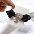 Detail eines eleganten schwarzen Haargummis mit Strass-Mittelstück und weißer Perle - Schwarz
