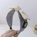 Detail eines Stoff-Stirnbands mit schwarz-weißem Karomuster und cremefarbener Schleife - Beige