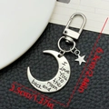 Détail du porte-clés lune argenté avec gravure et breloque étoile sur fond en cuir noir - Style Boucle de Porte Lettre Lune