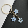 Porte-clés doré avec trois pendentifs fleurs de cerisier bleu clair sur un fond bicolore - Bleu