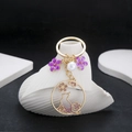 Detailed close-up of golden cat wreath keychain with purple cherry blossoms and pearl - Purple Oil-Drip Cat (ER718)
