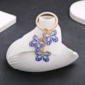 Details von drei blauen Emaille-Schmetterlingsanhängern an einem goldenen Schlüsselanhänger - Blauer Schmetterling (ER714)