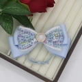 Detailed shot of a light blue bow hair tie with tweed fabric and pearl button detail - Blue