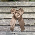 Gros plan d'une pince à cheveux nœud en satin marron avec rubans sur bois texturé - Marron 850