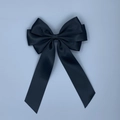 Détail d'une grande pince à cheveux en satin noir avec de longs rubans sur fond bleu-gris - Noir
